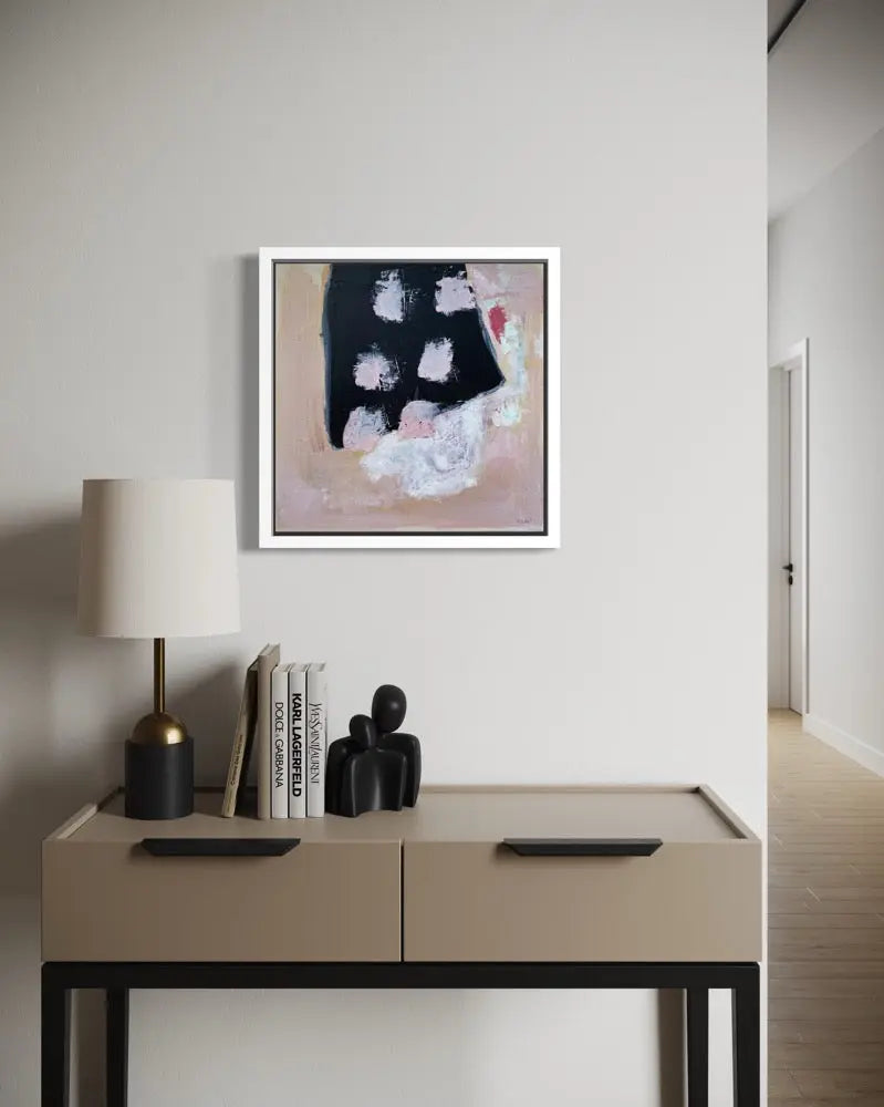 Beige side table with lamp, books, and decorative items against a white wall with abstract art.