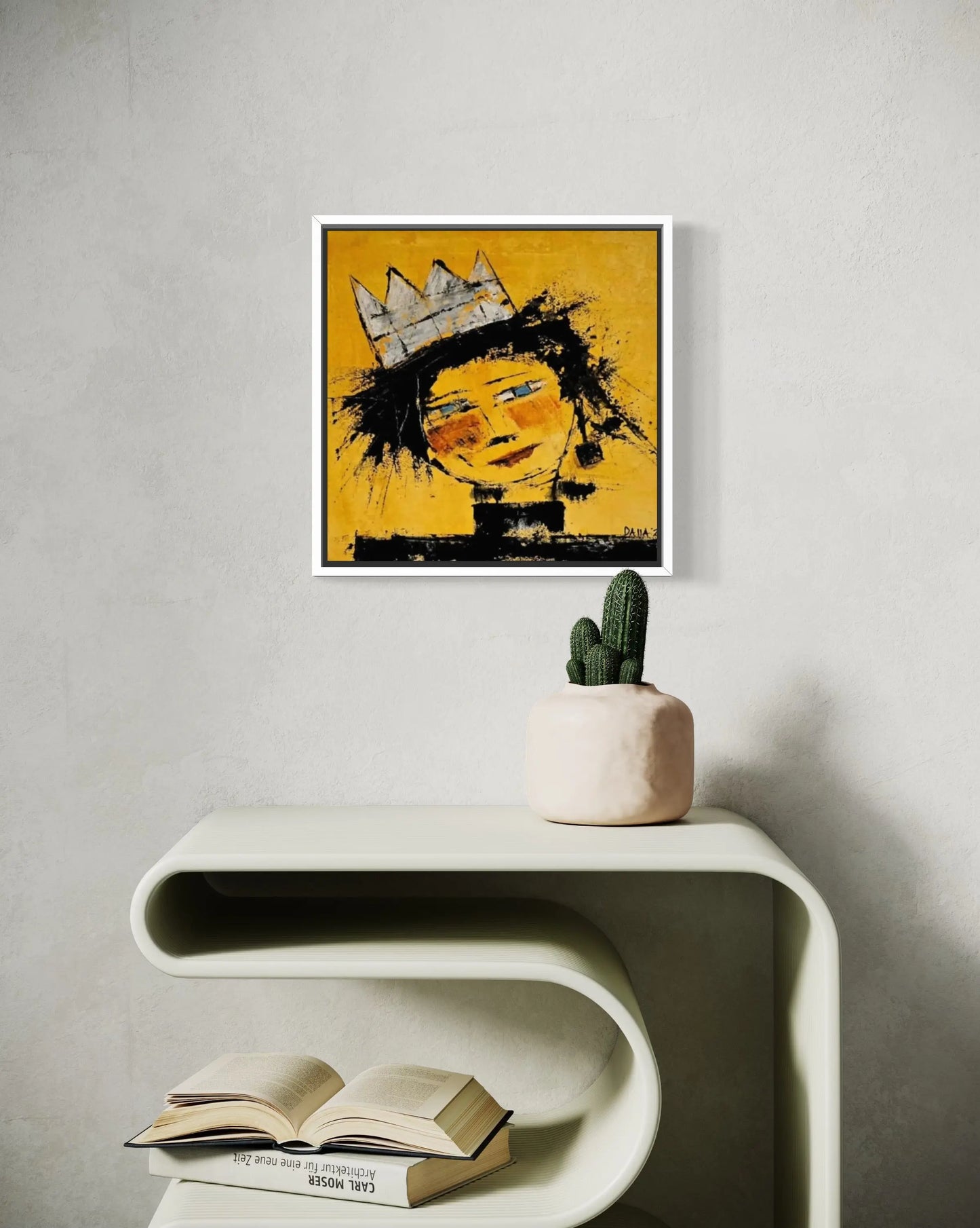Dalla myndlist, Untitled. Framed abstract artwork of a face with a crown on a wall above a white console table with books and a cactus.