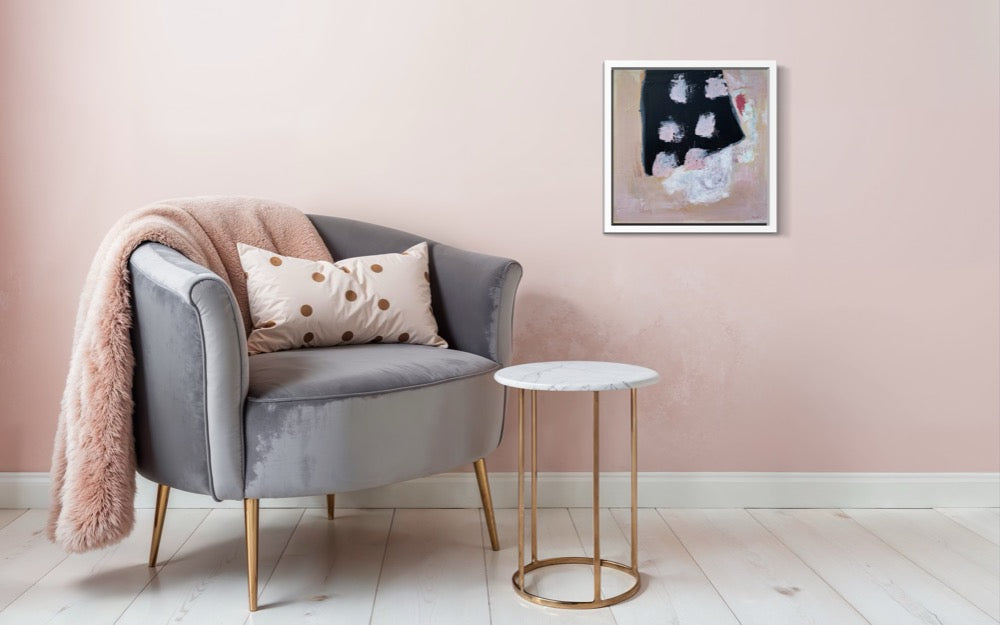Gray armchair with pink blanket and pillow, white side table, and abstract painting on pink wall.
