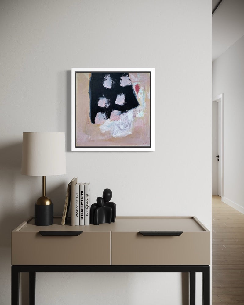 Beige side table with lamp, books, and decorative items against a white wall with abstract art.