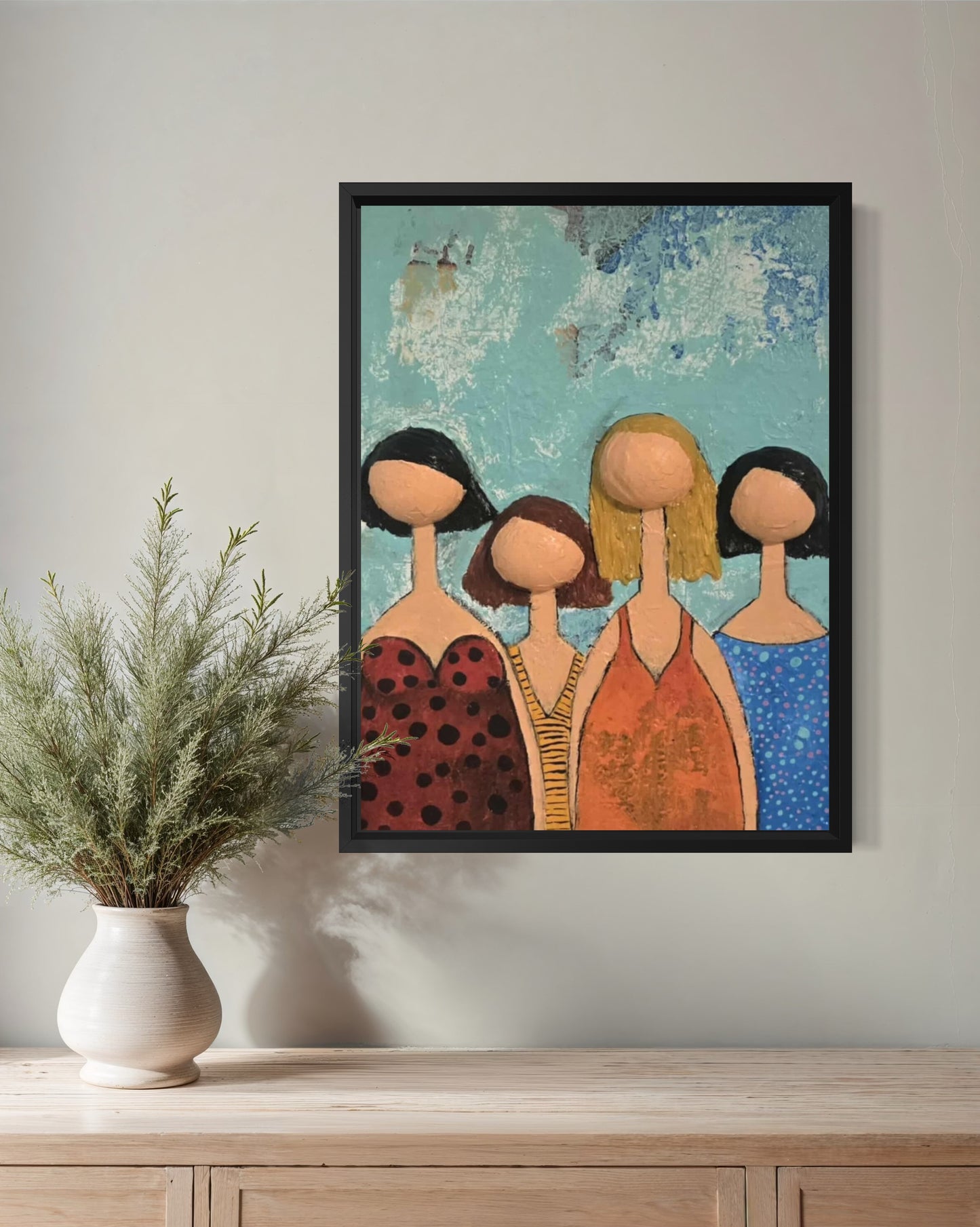 Dalla myndlist, Untitled. Framed artwork of four stylized figures on a wall above a wooden surface with a plant.