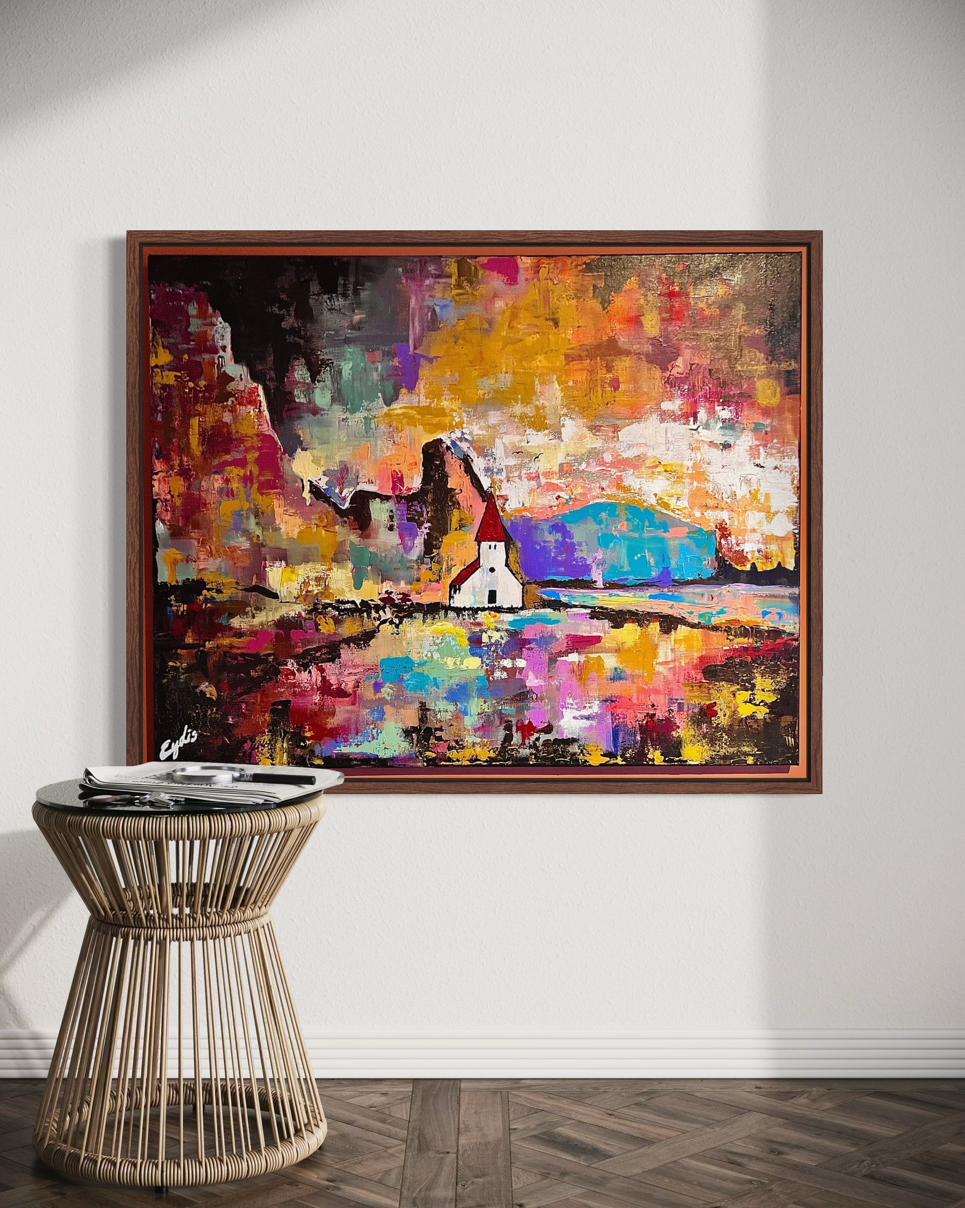 Colorful abstract Icelandic painting on a wall above a wicker side table.